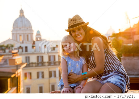 Portrait of happy mother and baby girl sitting on street overloo 17179213