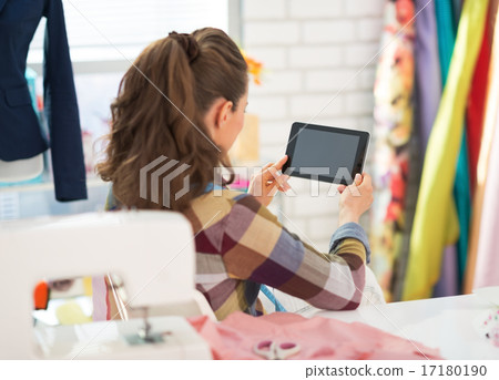 Seamstress using tablet pc at work. rear view Seamstress using tablet pc at work. rear view 17180190