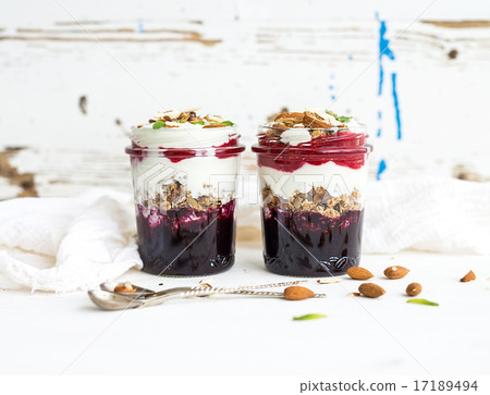 Yogurt oat granola with berries, honey and nuts in glass jars, rustic white background Yogurt oat granola with berries, honey and nuts in glass jars, rustic white background 17189494