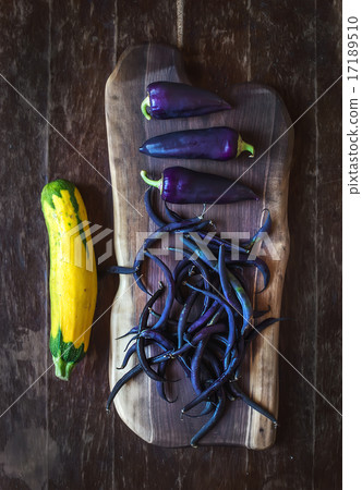 Violet chili peppers, beans and yellow zucchini on rustic wooden chopping board over dark wood 17189510