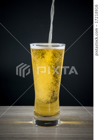 a beer pouring in a glass on a wood table a beer pouring in a glass on a wood table 17218916