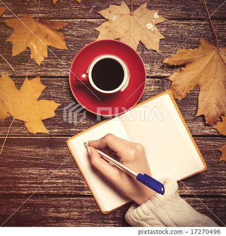 Female hand writing something in notebook near cup of coffee. 17270496