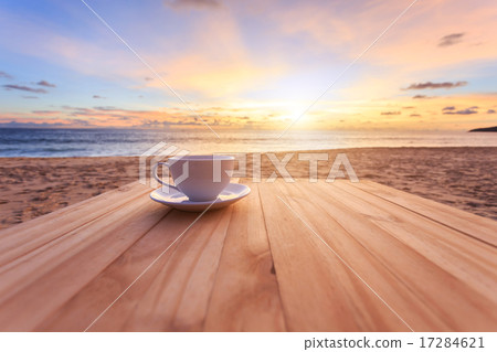 Coffee cup on wood table at sunset or sunrise beach Coffee cup on wood table at sunset or sunrise beach 17284621
