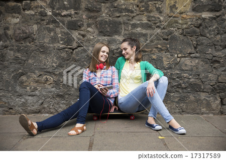 Two fashionable women sitting on skateboard. 17317589