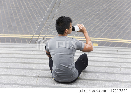 Asian man drinking while exercising outdoors. 17317851