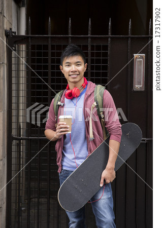 Chinese man with skateboard, standing outdoors. 17317902