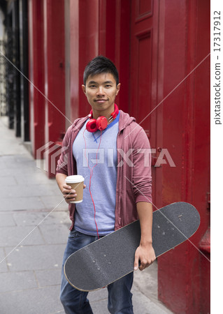 Chinese man with skateboard, standing outdoors. 17317912