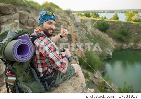 Young caucasian man with backpack sitting on the top of hill Young caucasian man with backpack sitting on the top of hill 17331918