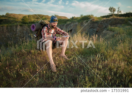 Young caucasian man with backpack sitting on the top of hill Young caucasian man with backpack sitting on the top of hill 17331991