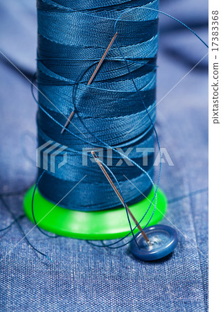 thread bobbin with needles, button on blue textile 17383368