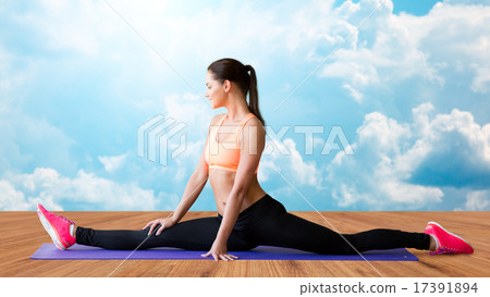 smiling woman doing splits on mat over clouds 17391894