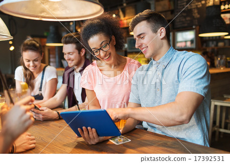 happy friends with tablet pc and drinks at bar 17392531