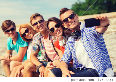 group of smiling friends with smartphone outdoors 17392833