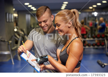 smiling woman with trainer and clipboard in gym 17393323