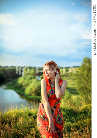 Young red-haired woman on the rock near river is fashionable poses in sunset time 17411700