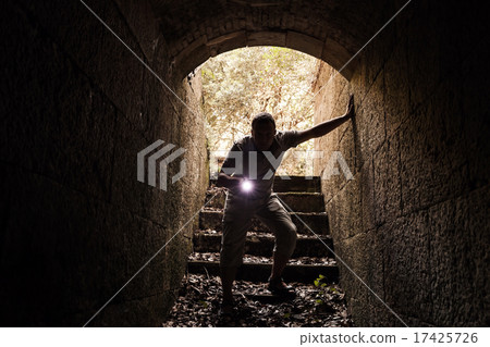 Young man with flashlight enters the stone tunnel 17425726