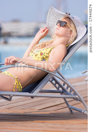 Young woman in swimsuit laying on chaise-longue poolside 17444874