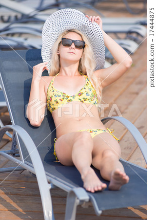 Young woman in swimsuit laying on chaise-longue poolside 17444875