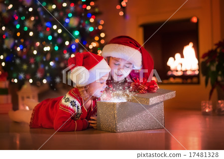 Kids opening Christmas presents at fireplace Kids opening Christmas presents at fireplace 17481328