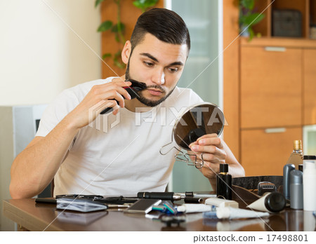 guy looking at mirror and shaving beard with trimmer 17498801