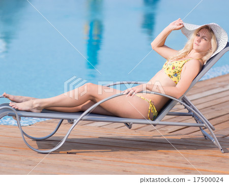 Young woman in swimsuit laying on chaise-longue poolside Young woman in swimsuit laying on chaise-longue poolside 17500024
