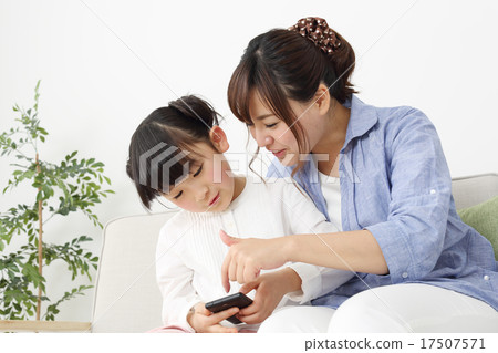 一個女孩誰玩智能手機和一位母親看著它 17507571