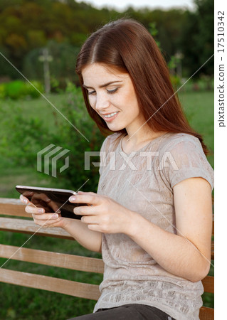 Young woman in a park texting on the tablet Young woman in a park texting on the tablet 17510342