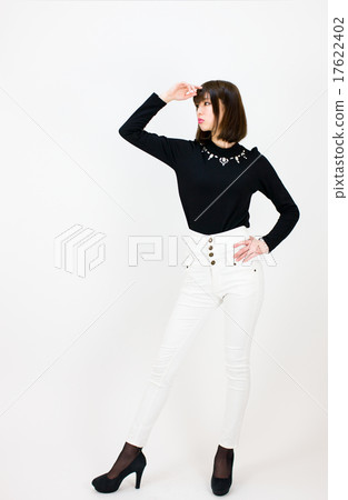 一個穿著白色褲子（褲子）的白色褲子（褲子）的年輕女子，通過將他的右手放在白色背景前的額頭上並將左手放在腰上，遠遠望去 17622402