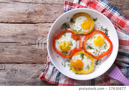 圖庫照片: fried eggs in peppers in a pan. top view