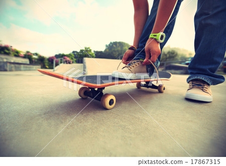 skateboarder tying shoelace at skatepark 17867315
