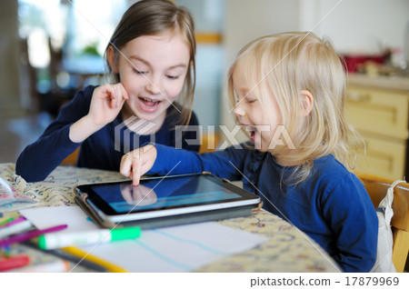 Two little sisters playing with a digital tablet Two little sisters playing with a digital tablet 17879969