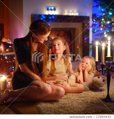 Young mother and daughters sitting by a fireplace on Christmas Young mother and daughters sitting by a fireplace on Christmas 17893435