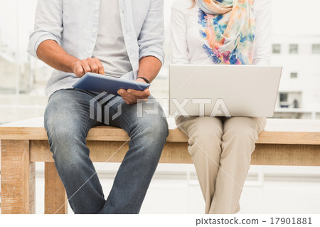 Casual designers sitting on wooden desk and using devices 17901881