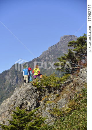 Three climbers looking up at the top of Ishizuruyama in fine weather Three climbers looking up at the top of Ishizuruyama in fine weather 17962725