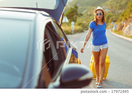 Woman with a yellow suitcase goes to a car parked on the roadsid Woman with a yellow suitcase goes to a car parked on the roadsid 17972895