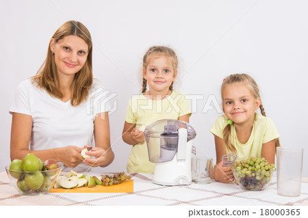 Mom and daughter sit at the table and cut fruit for juicing 18000365