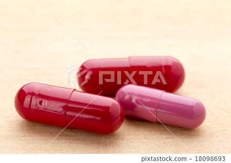 Three red capsules on the wooden table Three red capsules on the wooden table 18098693