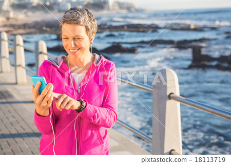Smiling sporty woman enjoying music and holding phone 18113719
