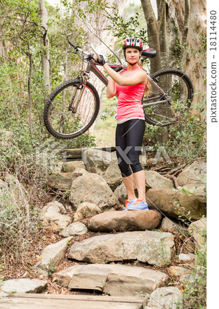 Blonde athlete carrying her mountain bike over rocks 18114480