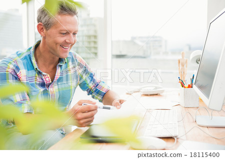 Smiling casual designer working at his desk Smiling casual designer working at his desk 18115400