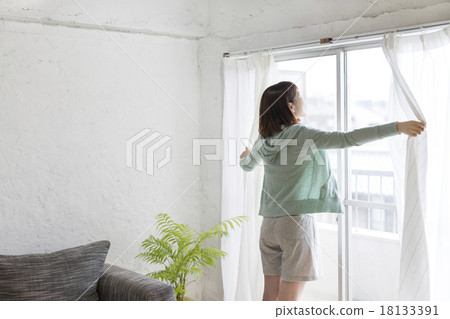 A young woman who opens a curtain 18133391