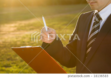 A businessman who fills the clipboard with the sunset behind the scenes A businessman who fills the clipboard with the sunset behind the scenes 18136583