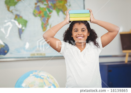 Smiling pupil balancing books on head in a classroom Smiling pupil balancing books on head in a classroom 18139865