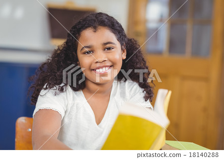 Smiling pupil reading book in a classroom Smiling pupil reading book in a classroom 18140288