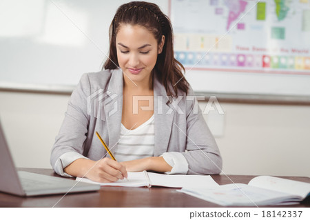 Pretty teacher correcting at her desk in a classroom Pretty teacher correcting at her desk in a classroom 18142337