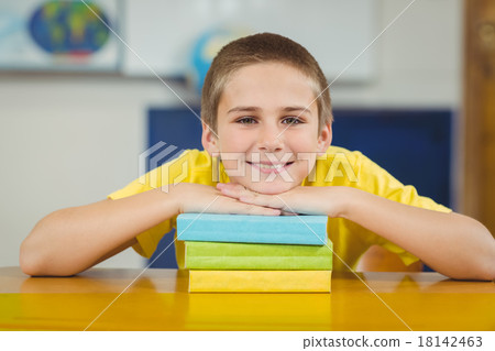 Smiling pupil leaning on pile of books in a classroom Smiling pupil leaning on pile of books in a classroom 18142463