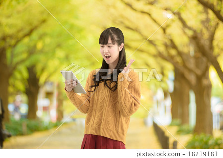 A young woman standing on a row of ginkgo biloba that beautifully colored leaves 18219181