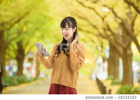 A young woman standing on a row of ginkgo biloba that beautifully colored leaves 18219183