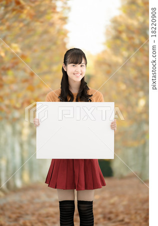 站立在秋天的死的葉子的一條美麗的沿途有樹的大道的少年婦女 18220908