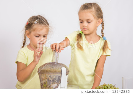 Two sisters squeezed fruit juice in a juicer 18242885